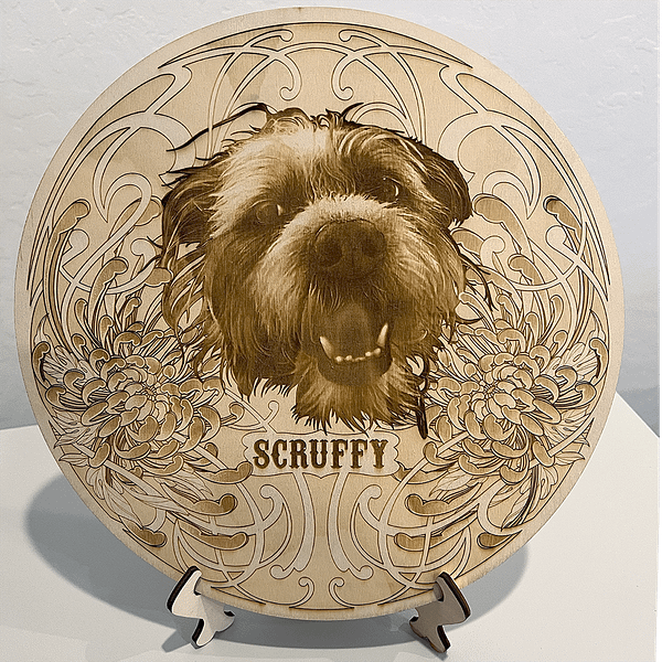 Laser Engraving of a Scruffy dog portrait framed in chrysanthemums on a poplar wood circle with the name Scruffy written underneath.